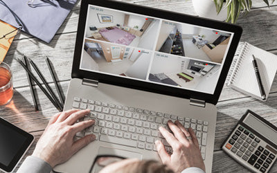 Person monitoring multiple home security camera feeds on a laptop in an office setting