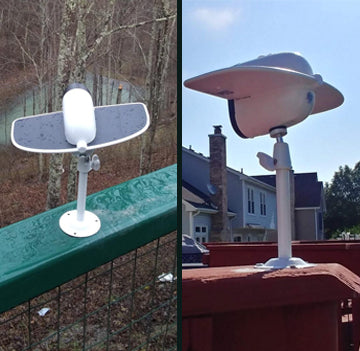 Two white weather sensors mounted on metal poles outdoors near houses and trees