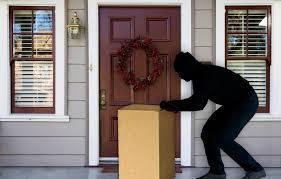 Person in black hoodie attempting to steal package from front porch with closed door