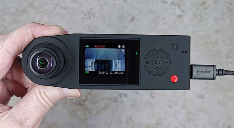 Hand holding a black Soliom dashcam with wide-angle lens and screen showing recorded footage
