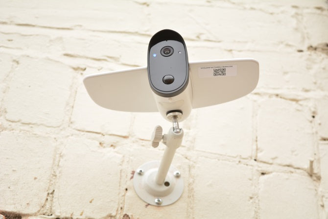 White security camera with black lens and sensor mounted on a white brick wall
