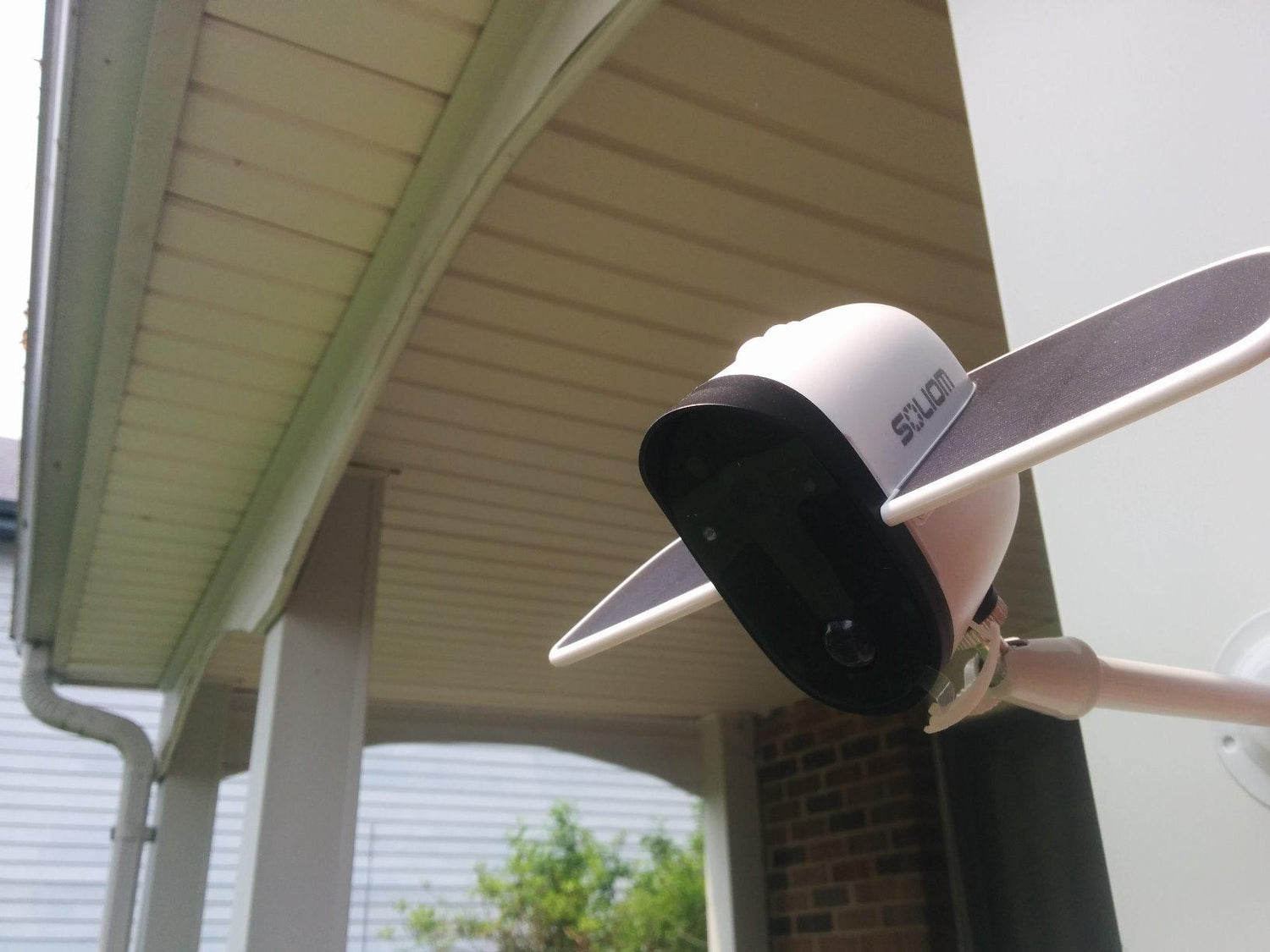 Wyze outdoor security camera mounted on a white house porch with roof and gutter visible