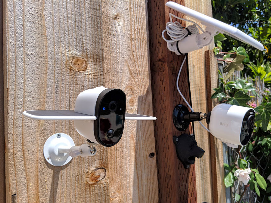 Arlo Pro 2 security cameras with white solar panels mounted on a wooden fence outdoors with green foliage