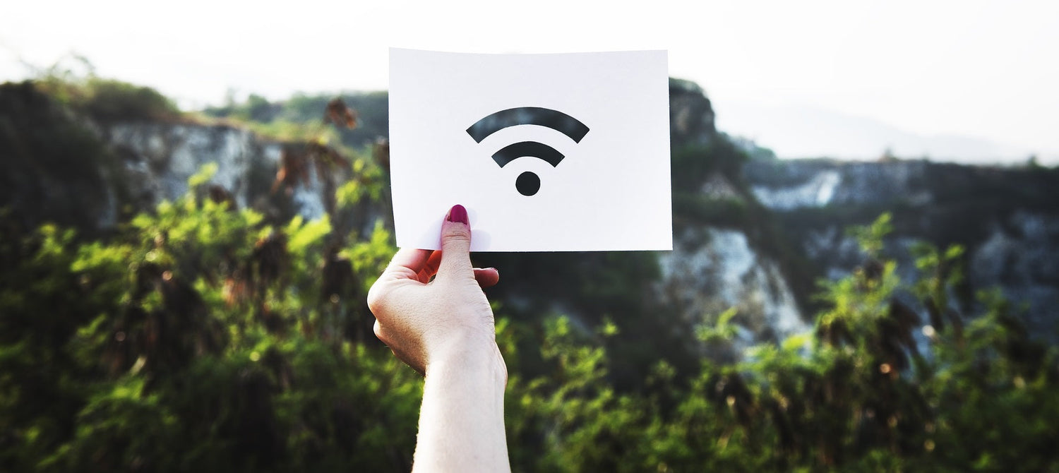 Hand holding paper with WiFi symbol outdoors with blurred green trees and hills background