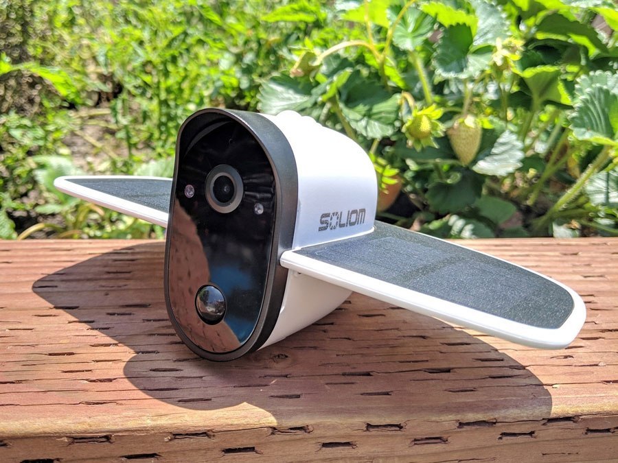 Soliom wireless solar-powered outdoor security camera with wings on wooden surface and green plants in background