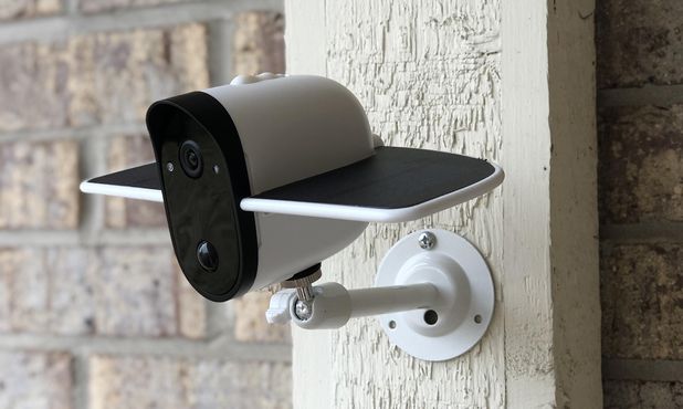 White outdoor security camera with sunshield mounted on textured beige wall with brick background