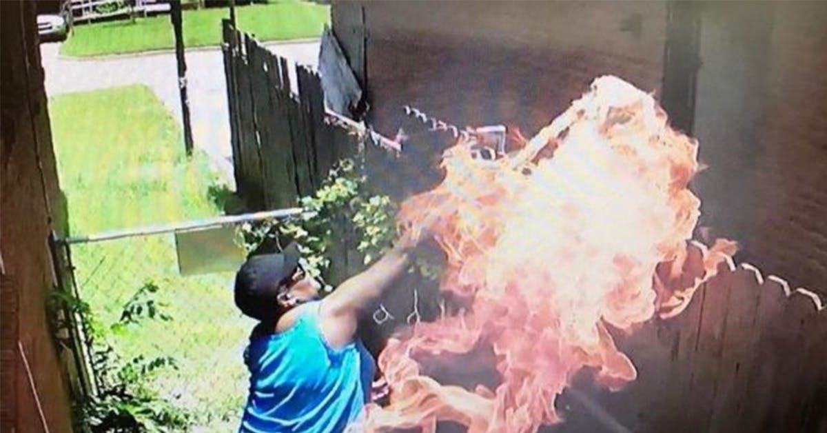 Person wearing blue sleeveless shirt spreading large flames near a wooden fence outdoors