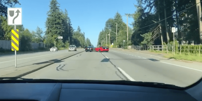 View from car dashboard on a sunny road with a red sports car and directional road sign