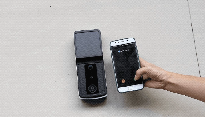 Hand holding smartphone showing incoming video call next to black video doorbell on wall