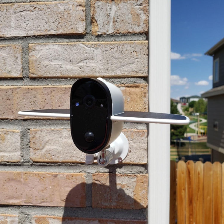 Outdoor security camera with solar panels mounted on brick wall under clear sky