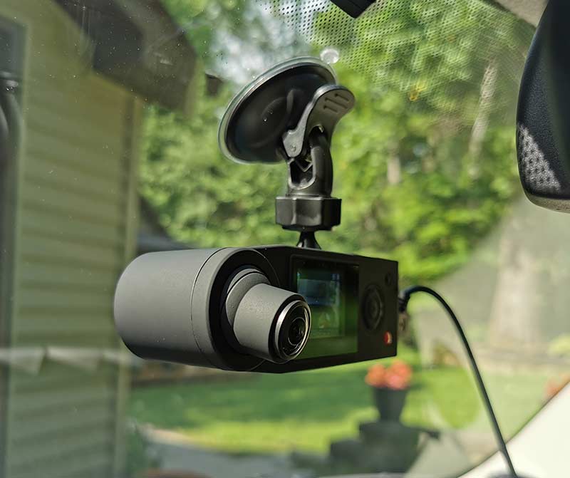 Black dashcam with wide lens mounted on car windshield using suction cup mount capturing outdoor scenery